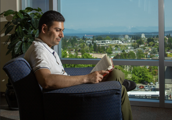 Man reading beside a window with an ocean view.