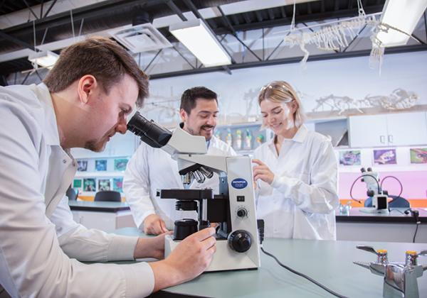 Group of people working in a lab. One person is looking through a microscope